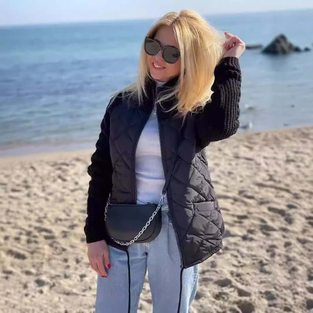 Woman wearing a stylish black stand collar jacket on the beach, featuring a knitted design and zipper, showcasing modern winter fashion.